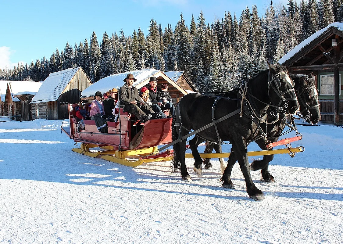 Two horses pull a red sleigh with a group of people through the snow.