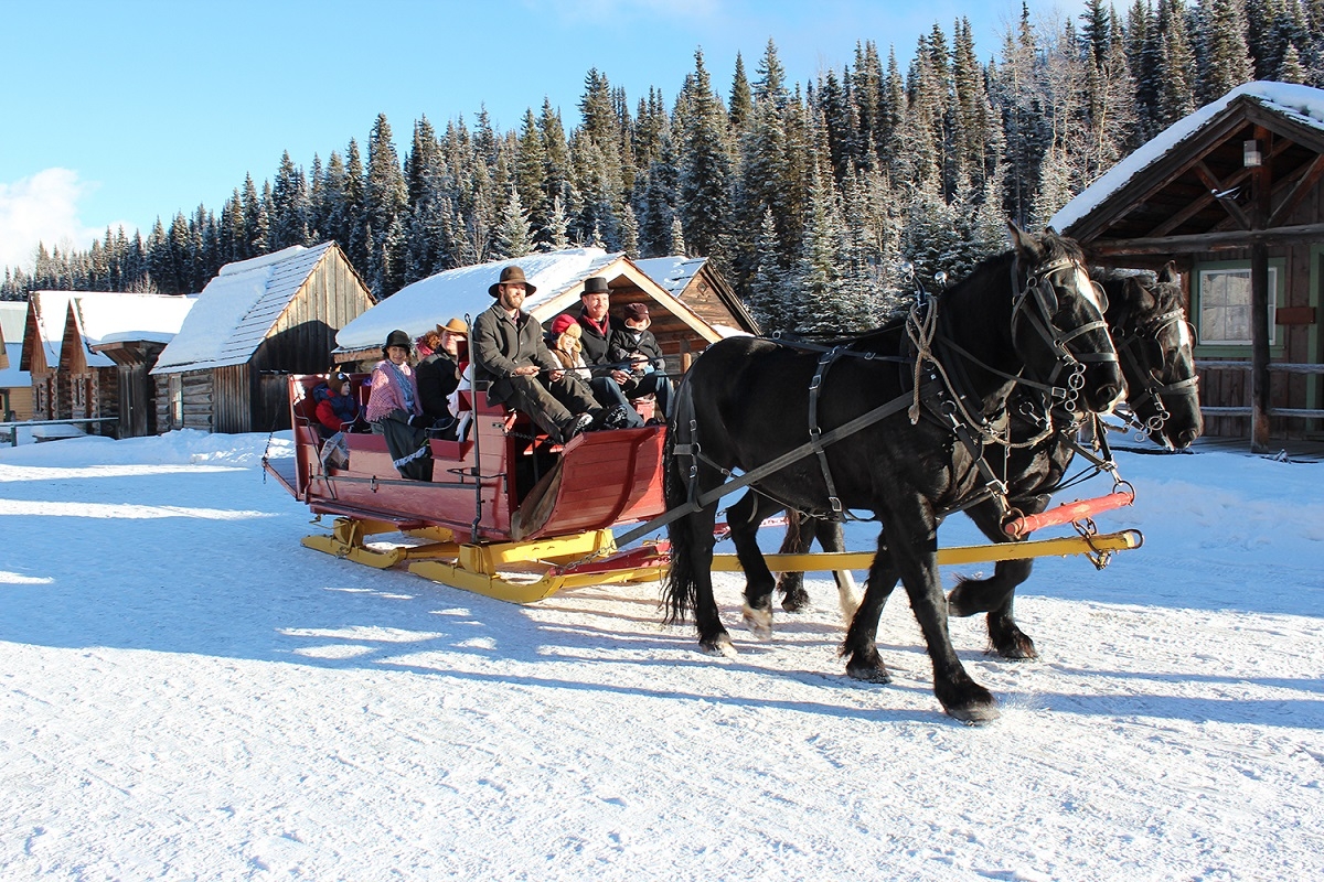 Two horses pull a red sleigh with a group of people through the snow.