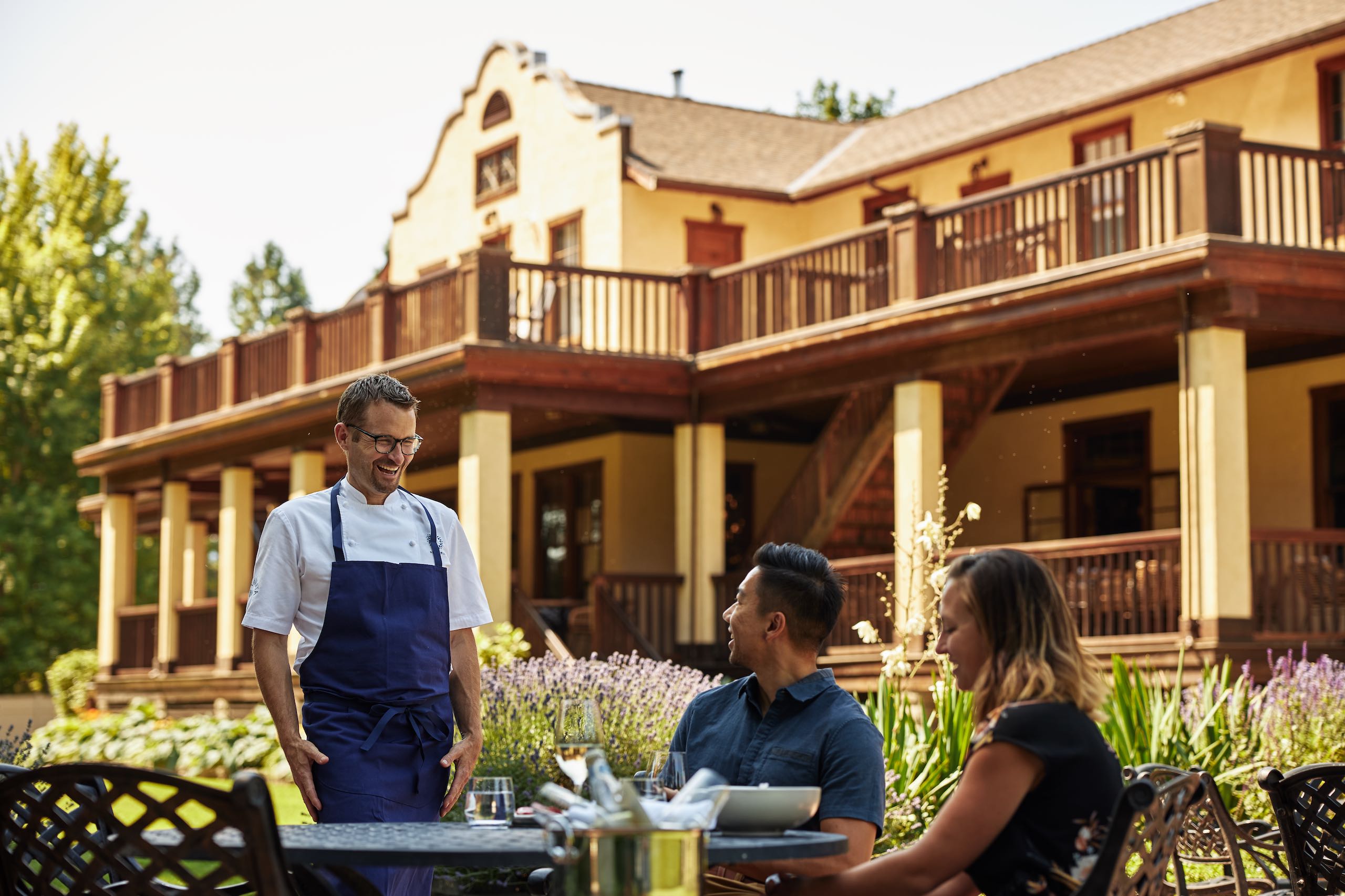 Chef Ned Bell describes the meal to two people dining on the patio at the Naramata Inn