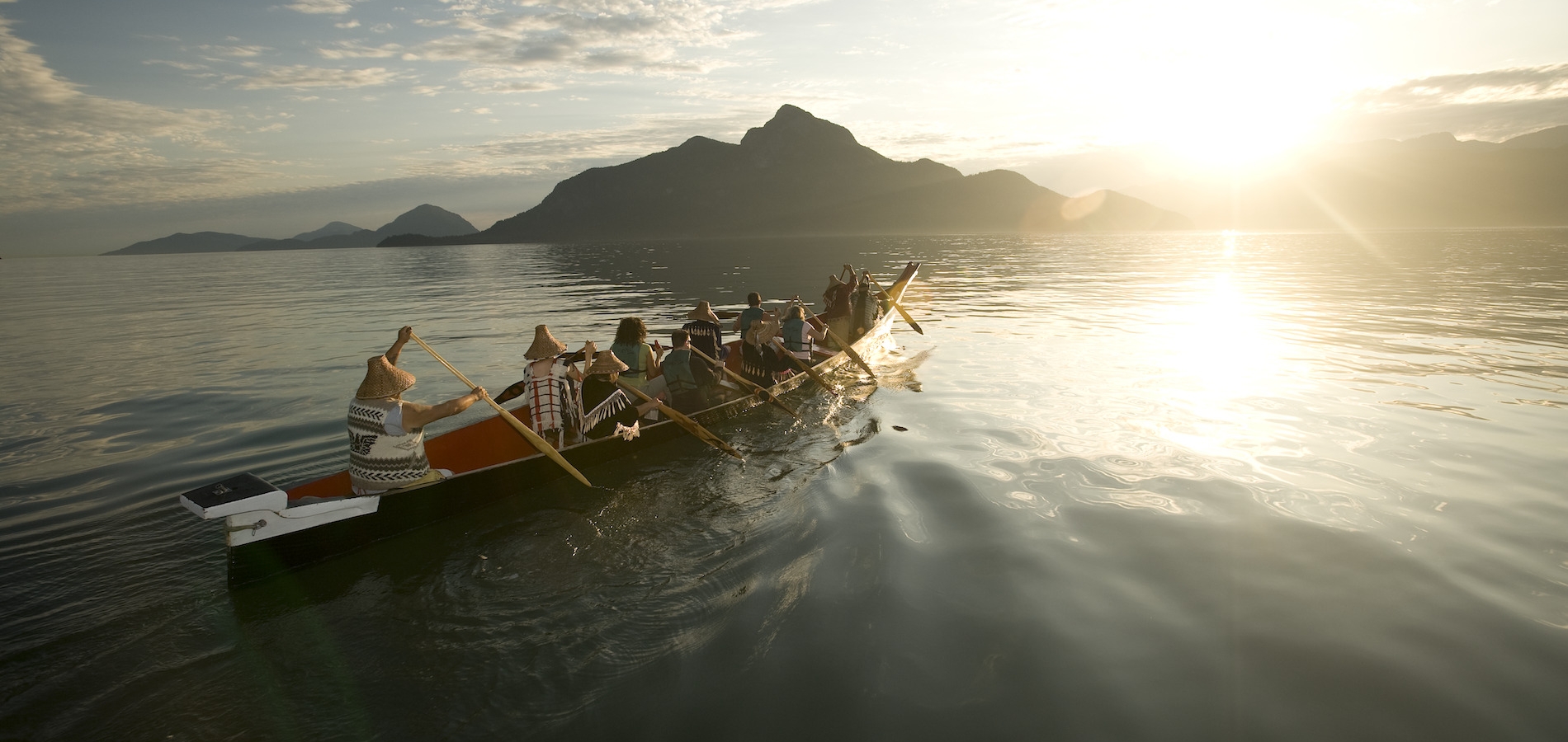 A group with Takaya Tours, rowing a traditional First Nations canoe in Howe Sound with mountains in the background.