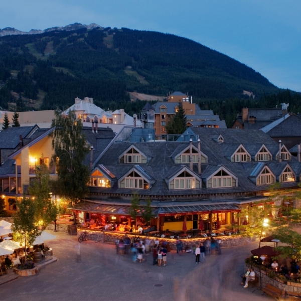 Aerial view of a pedestrian walkway in Whistler Village with hotels and retail space, and forested mountains in the background.
