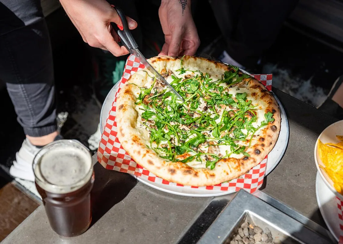 Una pizza que se está cortando con unas tijeras en una cervecería, con una cerveza al lado