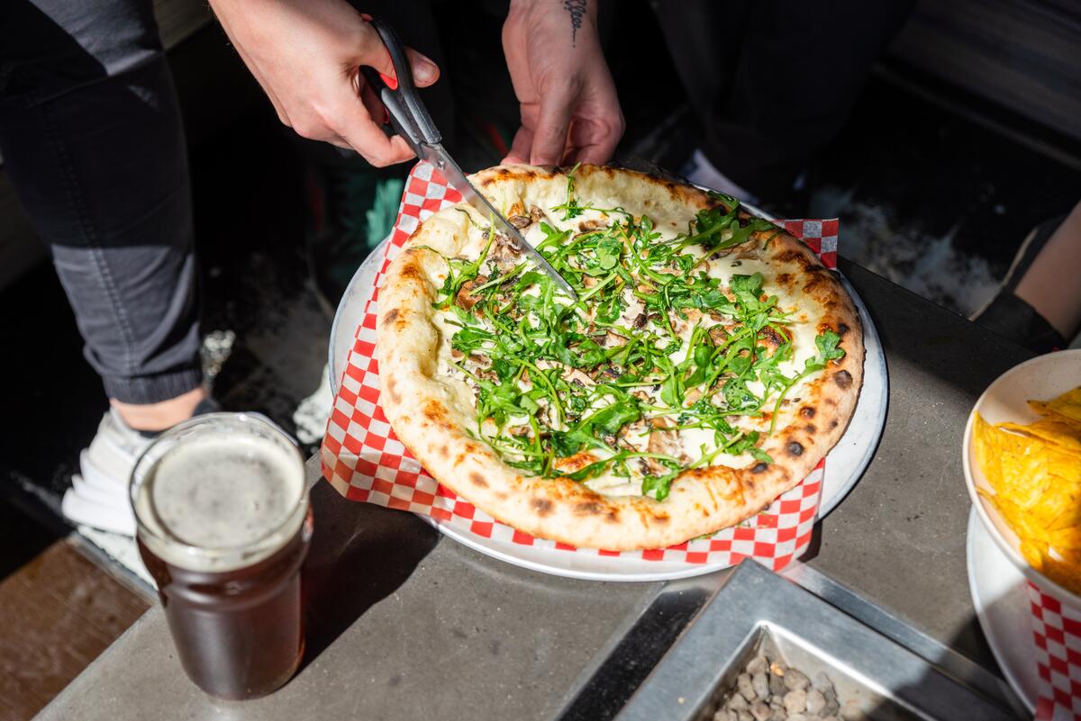 Pizza being cut with scissors at a brewery with a beer next to it