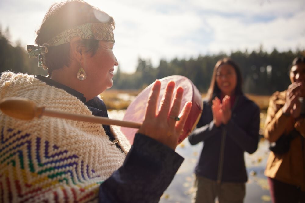 Candace Campo from Talaysay Walking Indigenous Tours is conducting a presentation and speaking to a group while on a walking experience in Stanley Park in Vancouver.