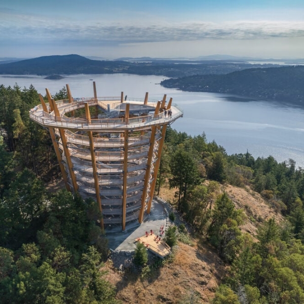 A spiralling walkway, narrower at the bottom, leads to views of the Salish Sea with forested islands visible in the distance.