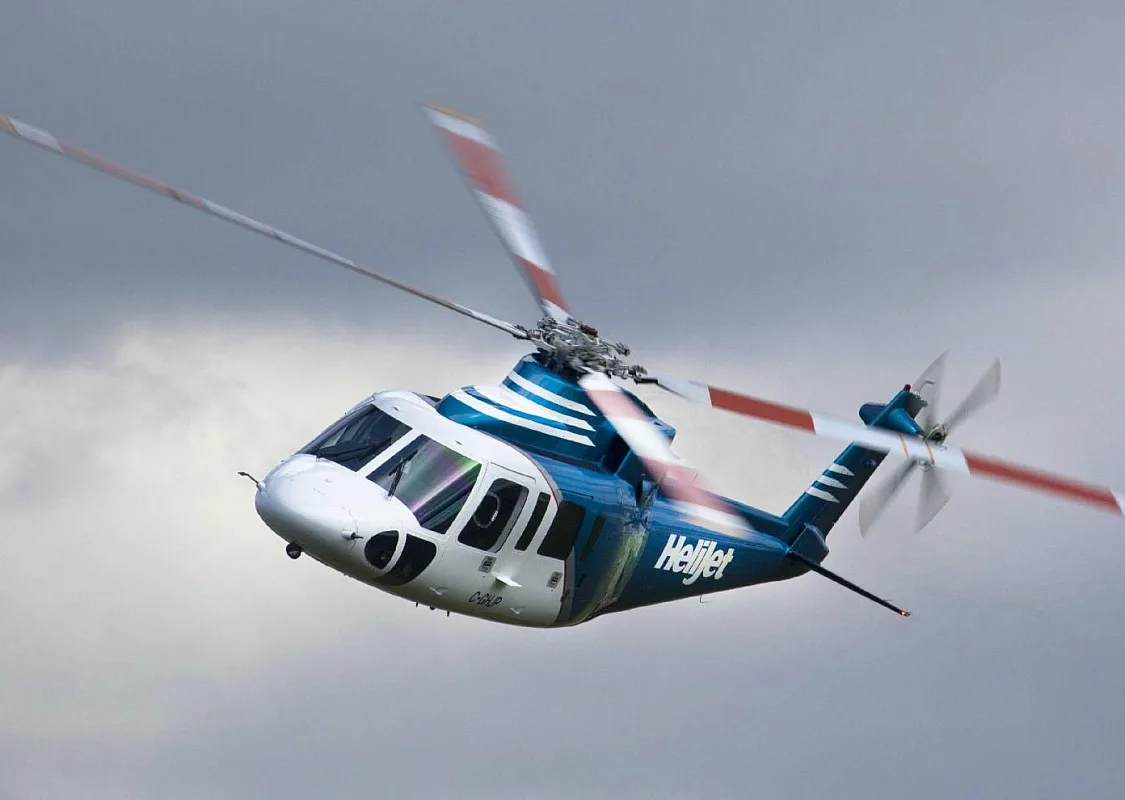 A helicopter by Helijet International flies against a cloudy sky
