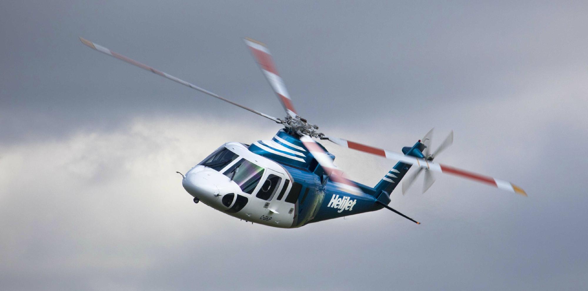 A helicopter by Helijet International flies against a cloudy sky