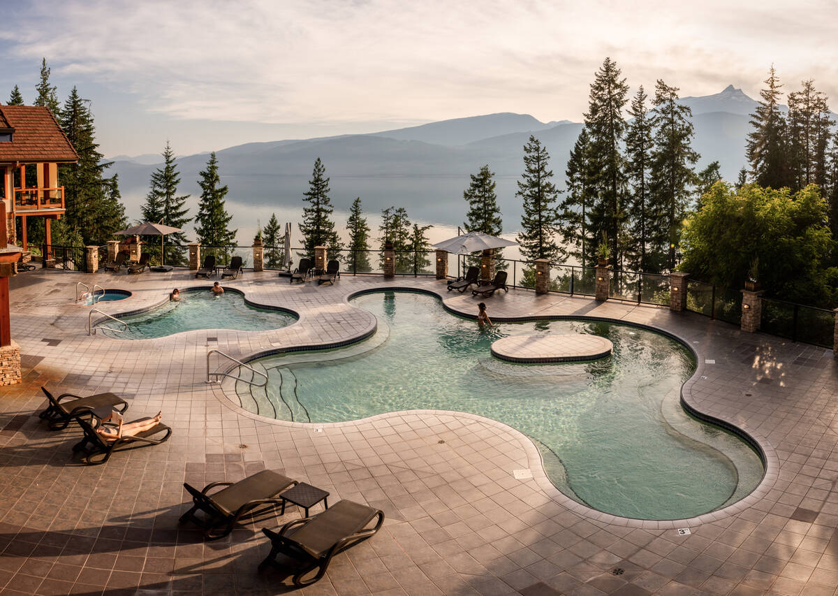 Pool deck with two hot springs pools, one big one small, the big one the shape of an amoeba. In the distance is a huge lake and mountains behind the lake.