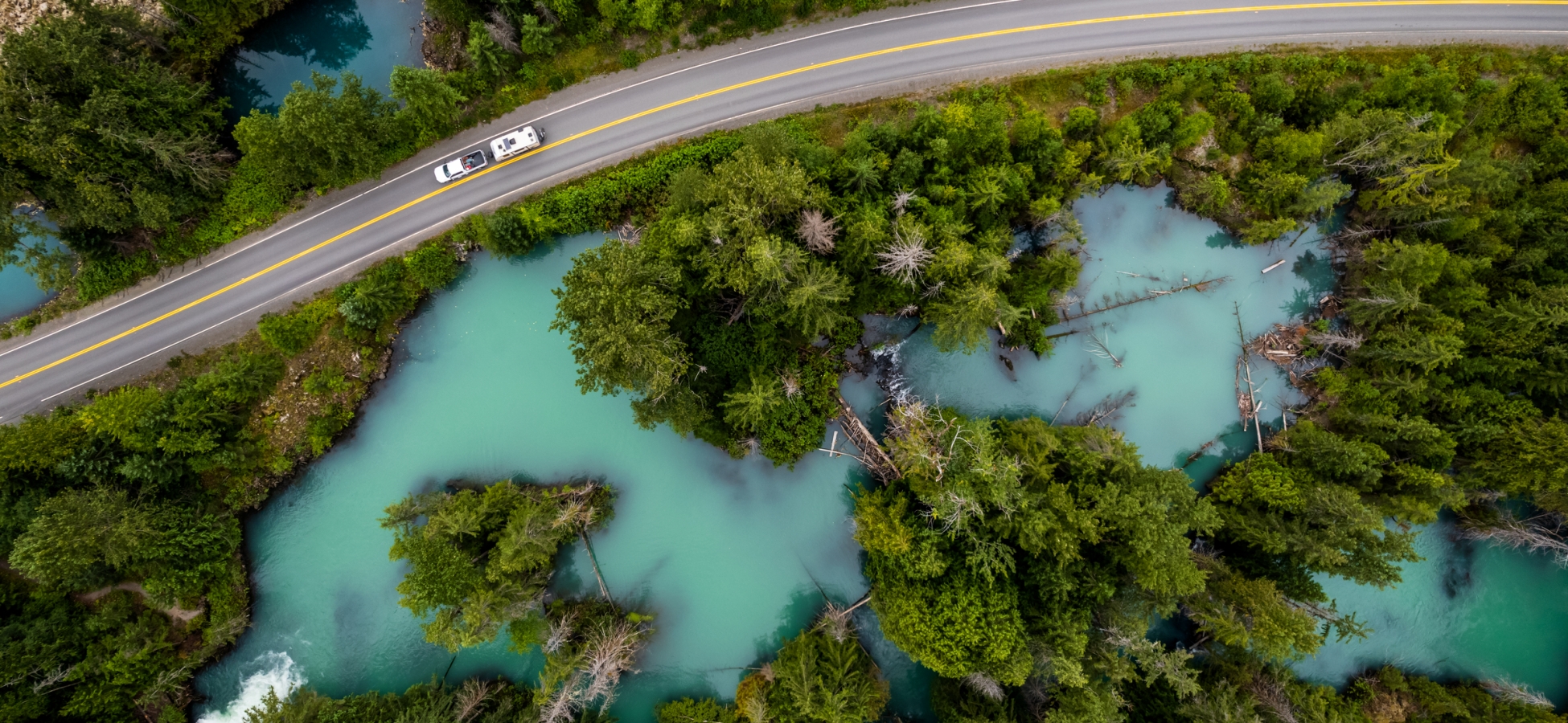 An aerial view of an RV driving through the Drowned Forest, a sea of turquoise water with forest growing into it.