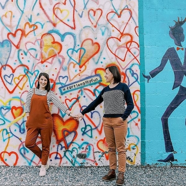 Two people hold hands in front of a colourful mural.