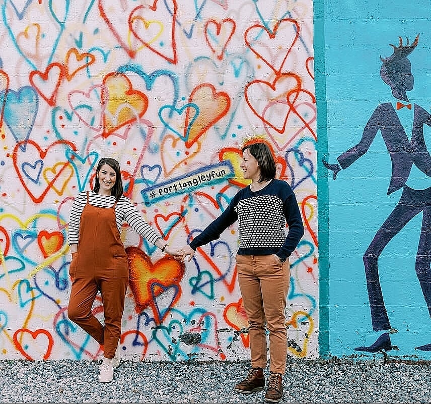 Two people hold hands in front of a colourful mural.
