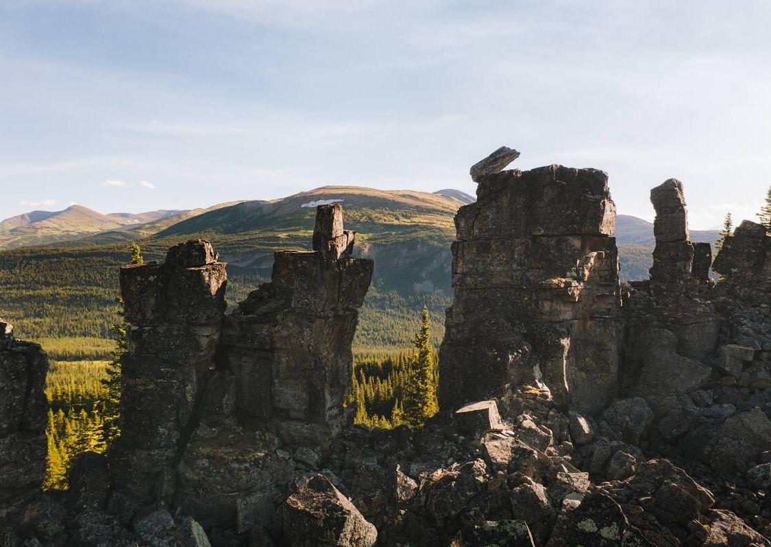 Eine Vielzahl von aufeinander gestapelten Felsen in Form von Schiffsschornsteinen mit einem üppigen borealen Wald im Hintergrund.
