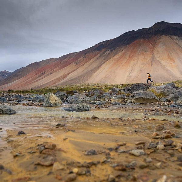 Dos corredores de senderos se ven pequeños en el contexto del imponente monte Edziza, con vetas de colores óxido y hueso.