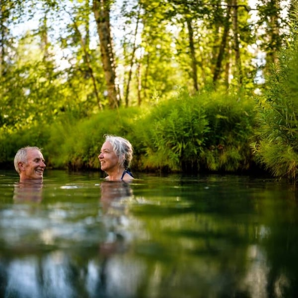 Una pareja de mediana edad se relaja en las aguas termales, rodeada de un bosque.