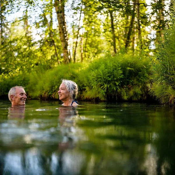 A middle-aged couple soaks in the hot springs, surrounded by forest.
