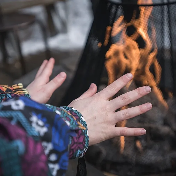 A person warms their hands by an outdoor electric fire. They are wearing a colourful patterned sweater.