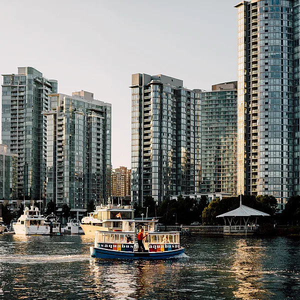 An Aquabus moves across the water from downtown Vancouver. Glass high rises and boats docked at the marina are in the background.