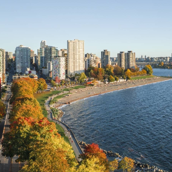 Aerial view over the ocean with a beach, trees, and highrise buildngs to the left.