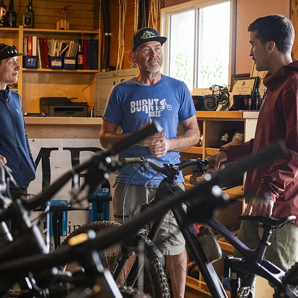 Three people stand inside a bike shop surrounded by bike apparel and gear.