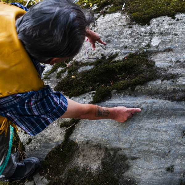 Clyde Anzac of the NIsga'a Nation points to dark rocks containing petroglyphs.