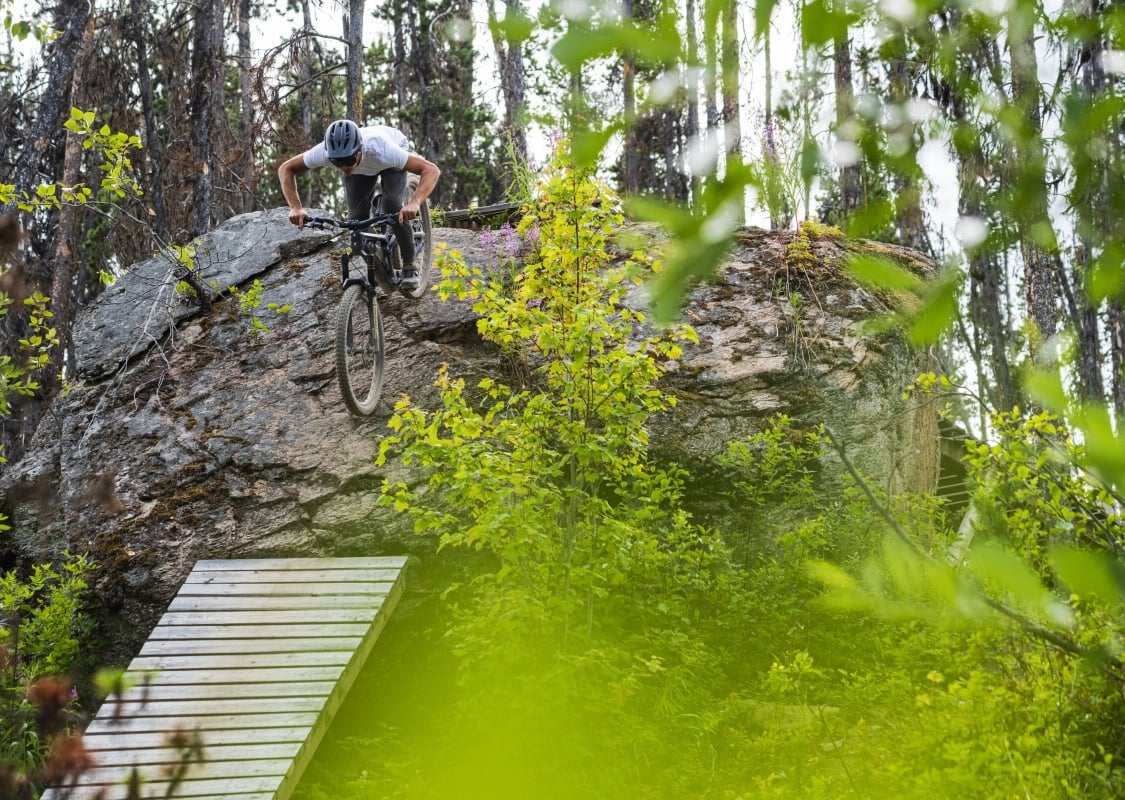 Un ciclista de montaña baja por una pared de roca con una escalera de madera debajo.