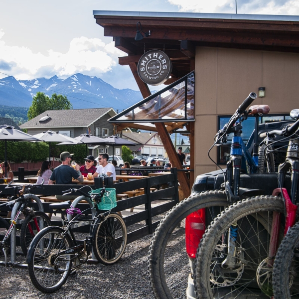 Un grupo de ciclistas de montaña disfruta de una cerveza de barril en el patio de una cervecería local con sus bicicletas estacionadas en frente.