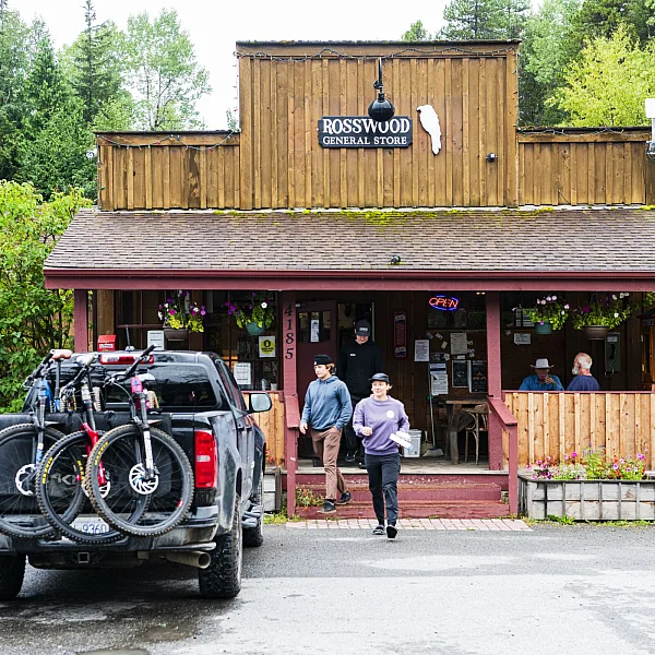 Two people walk out of a general store towards their truck, which is carrying mountain bikes.