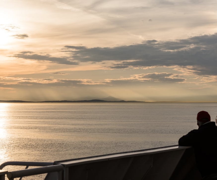 Couple watching the sunset on BC Ferries. They are leaning on the railing looking out at the ocean.