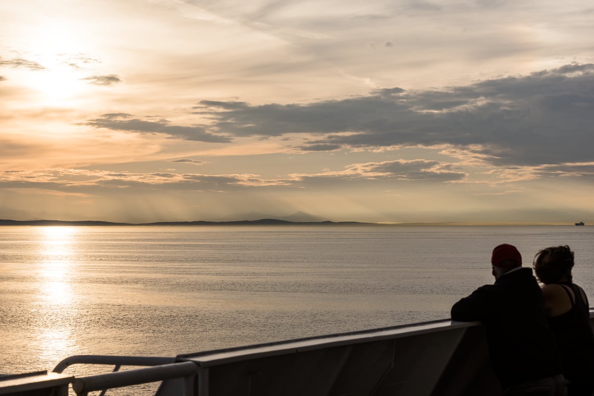 Couple watching the sunset on BC Ferries. They are leaning on the railing looking out at the ocean.