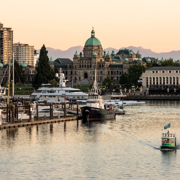 A water taxi moves through the water on the right with a marina on the left of the frame. Buildings are visible in the background, including the intricate legislature.