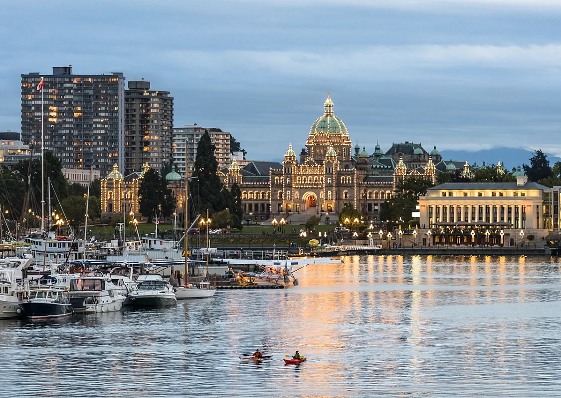 El frente del puerto del centro de Victoria por la noche. Las luces de los Edificios del Parlamento de la Columbia Británica están encendidas, reflejándose en el agua.