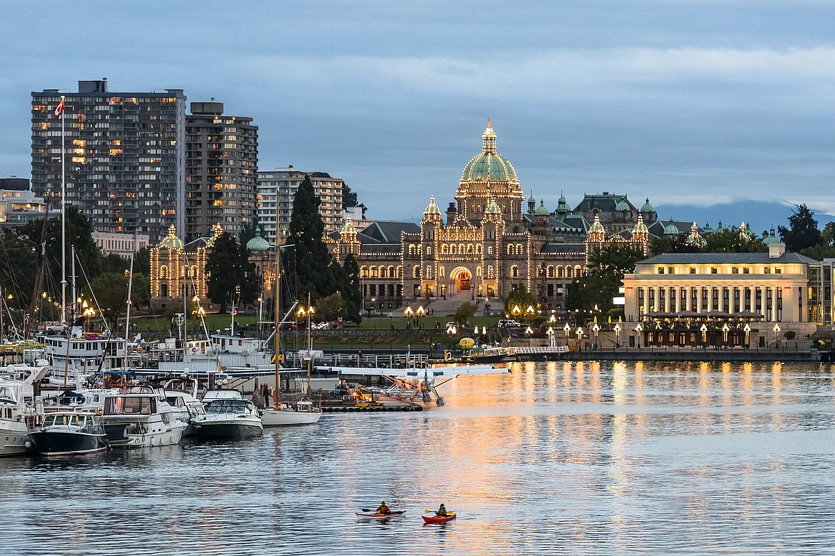 El frente del puerto del centro de Victoria por la noche. Las luces de los Edificios del Parlamento de la Columbia Británica están encendidas, reflejándose en el agua.