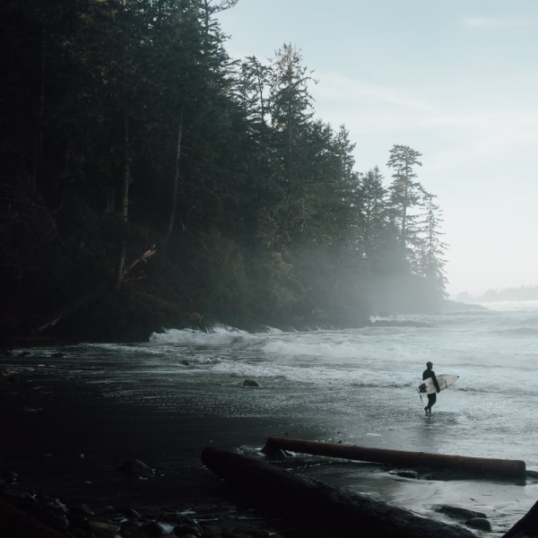 A person walks into the ocean holding a surfboard in Florencia Bay in Ucluelet