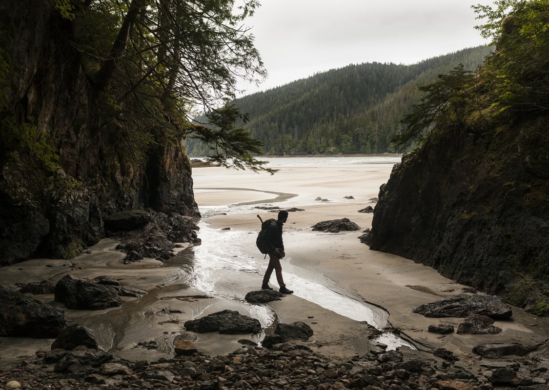 A person walks along a beach between two rocky outcrops.