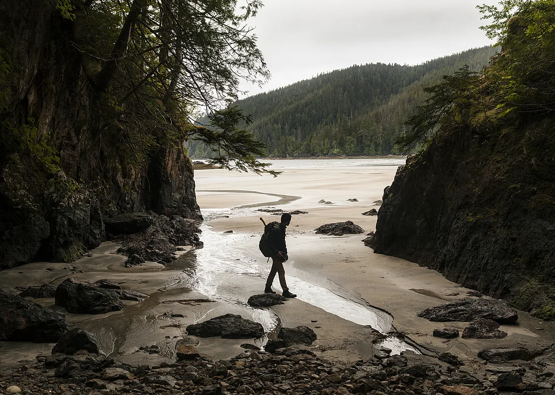 A person walks along a beach between two rocky outcrops.