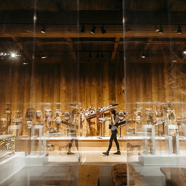 A person walks through the U'Mista Cultural Centre with Indigenous art on display behind glass panels | Nathan Martin