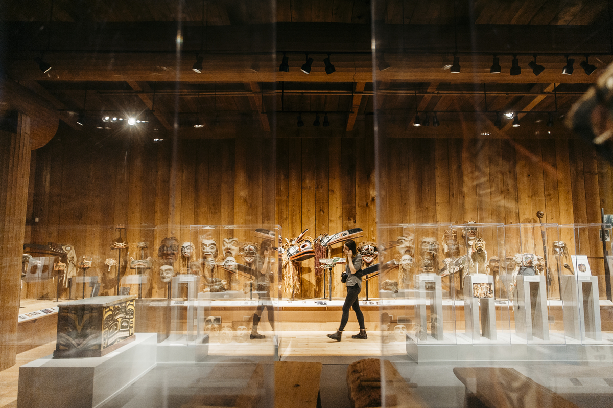 A person walks through the U'Mista Cultural Centre with Indigenous art on display behind glass panels | Nathan Martin