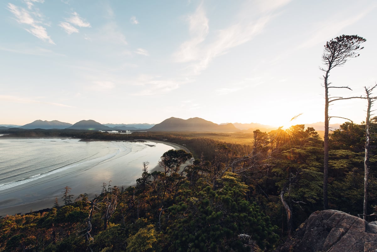 The sunsets over the ocean with the mountains in the distance in Tofino, BC