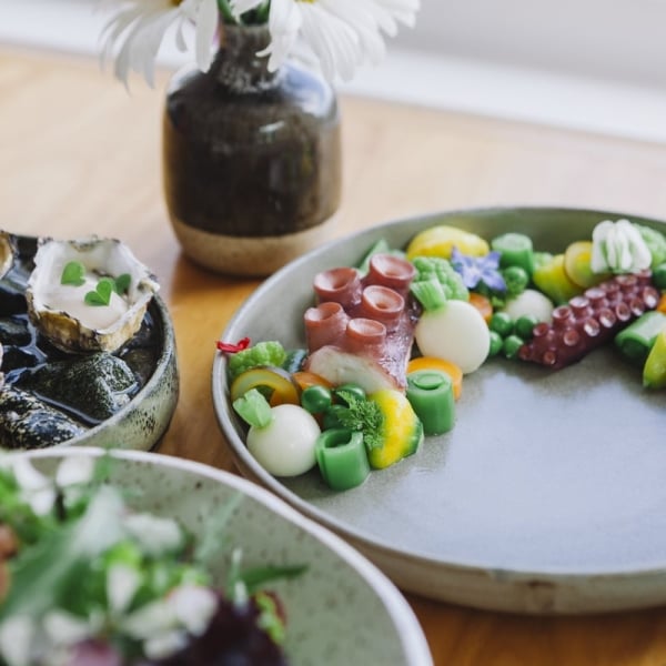 Three dishes of seafood on a wooden table with an assortment of sushi and other items.