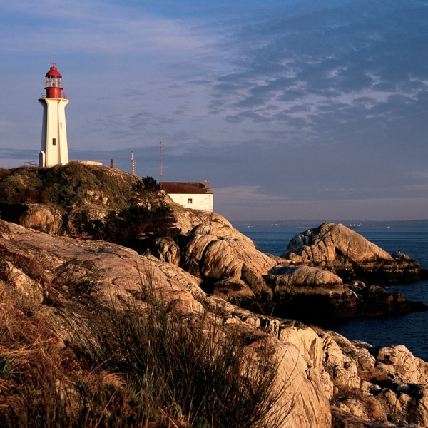 A red and white lighthouse sits on a rocky coastline at Lighthouse Park in West Vancouver. The sun is setting and the ocean is dark