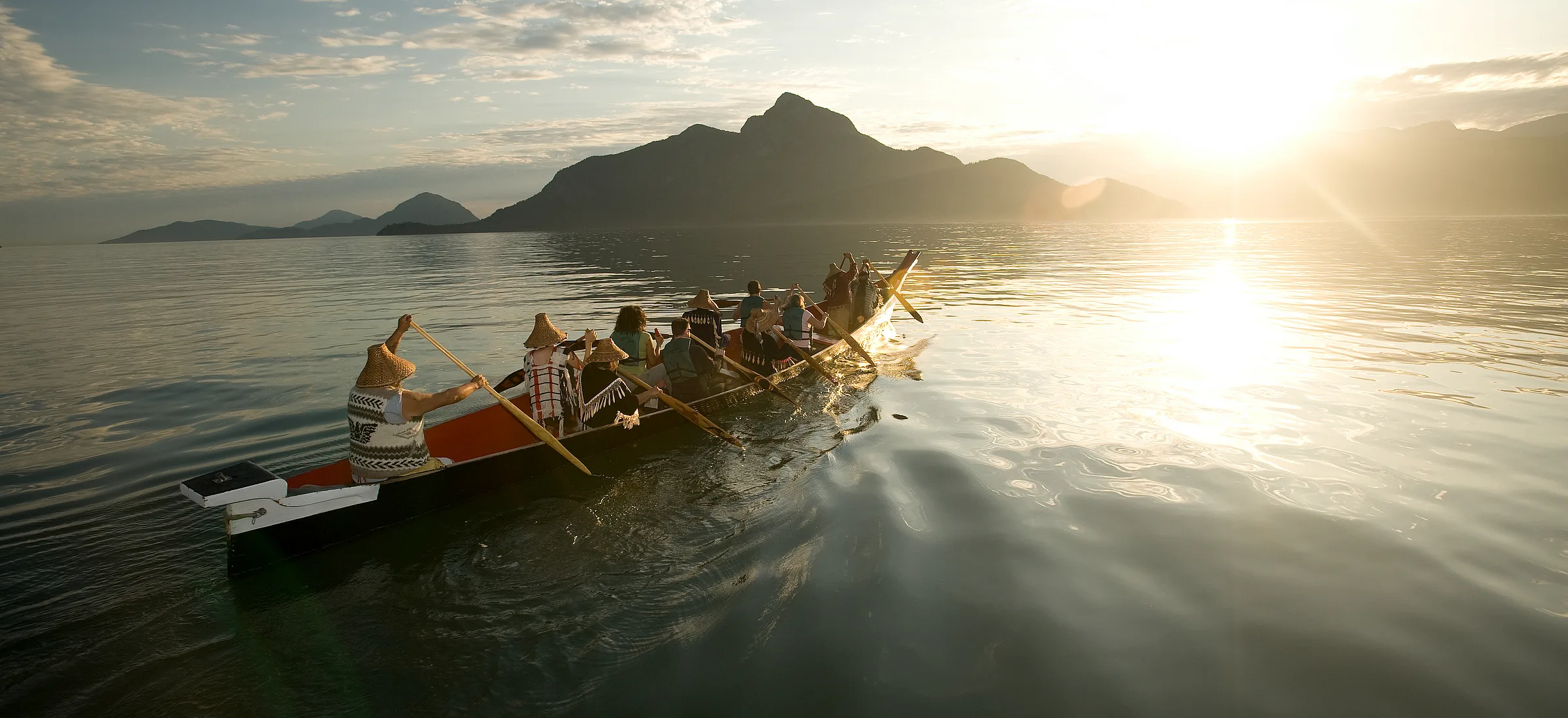 Un grupo con Takaya Tours, remando una canoa tradicional de las Primeras Naciones en Howe Sound con montañas al fondo.