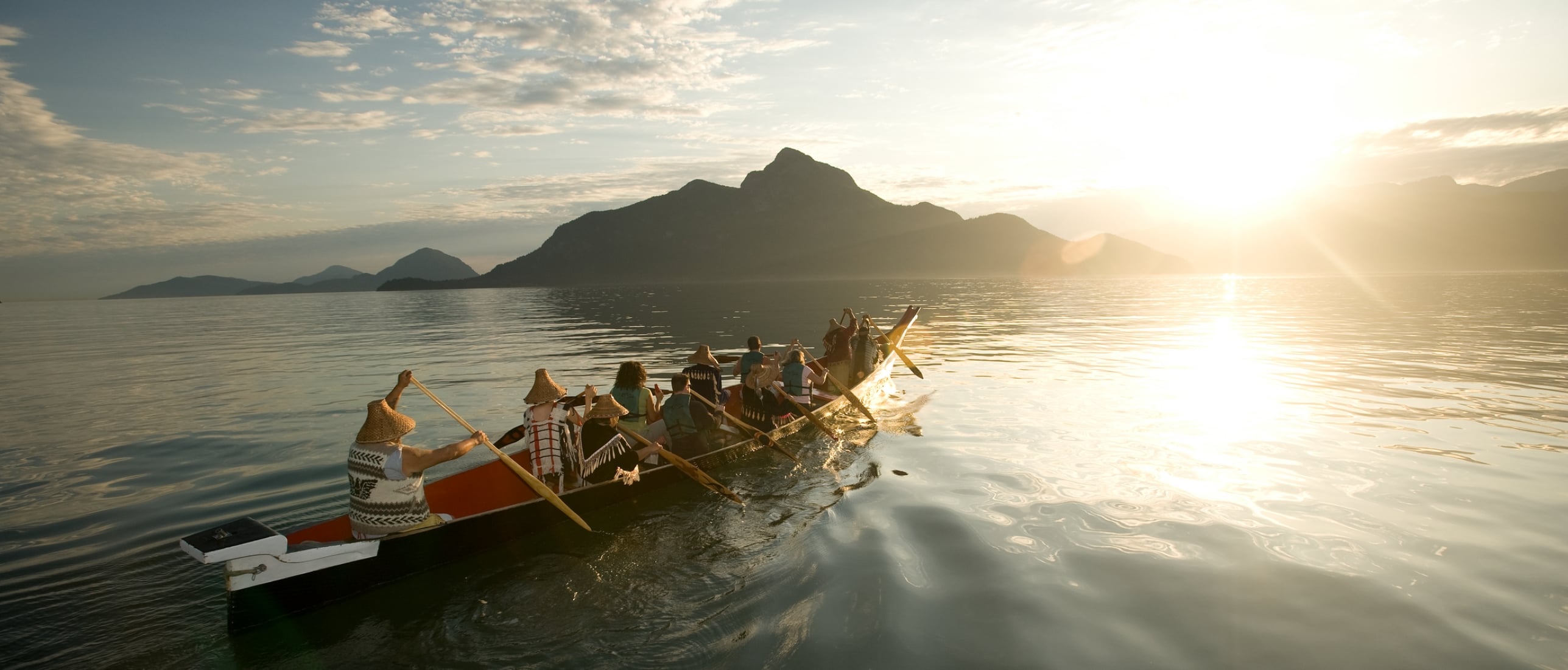 A group with Takaya Tours, rowing a traditional First Nations canoe in Howe Sound with mountains in the background.