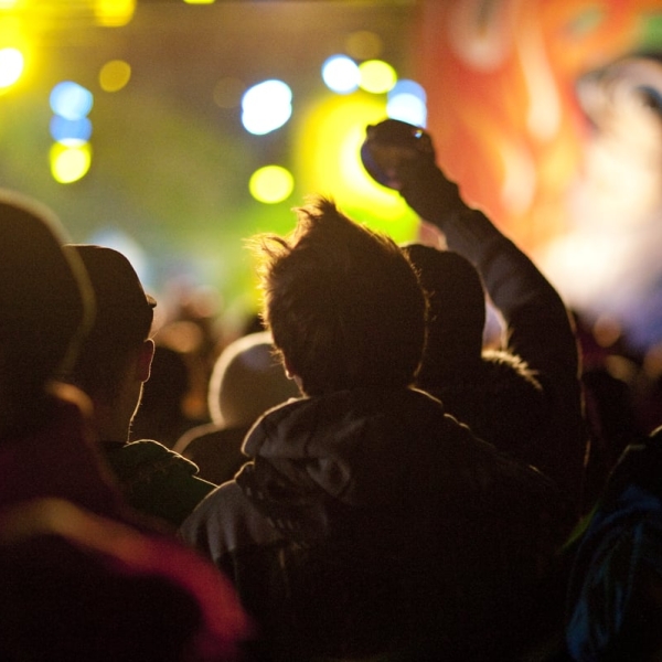 A crowd of people watches a live performance with lights and projections.