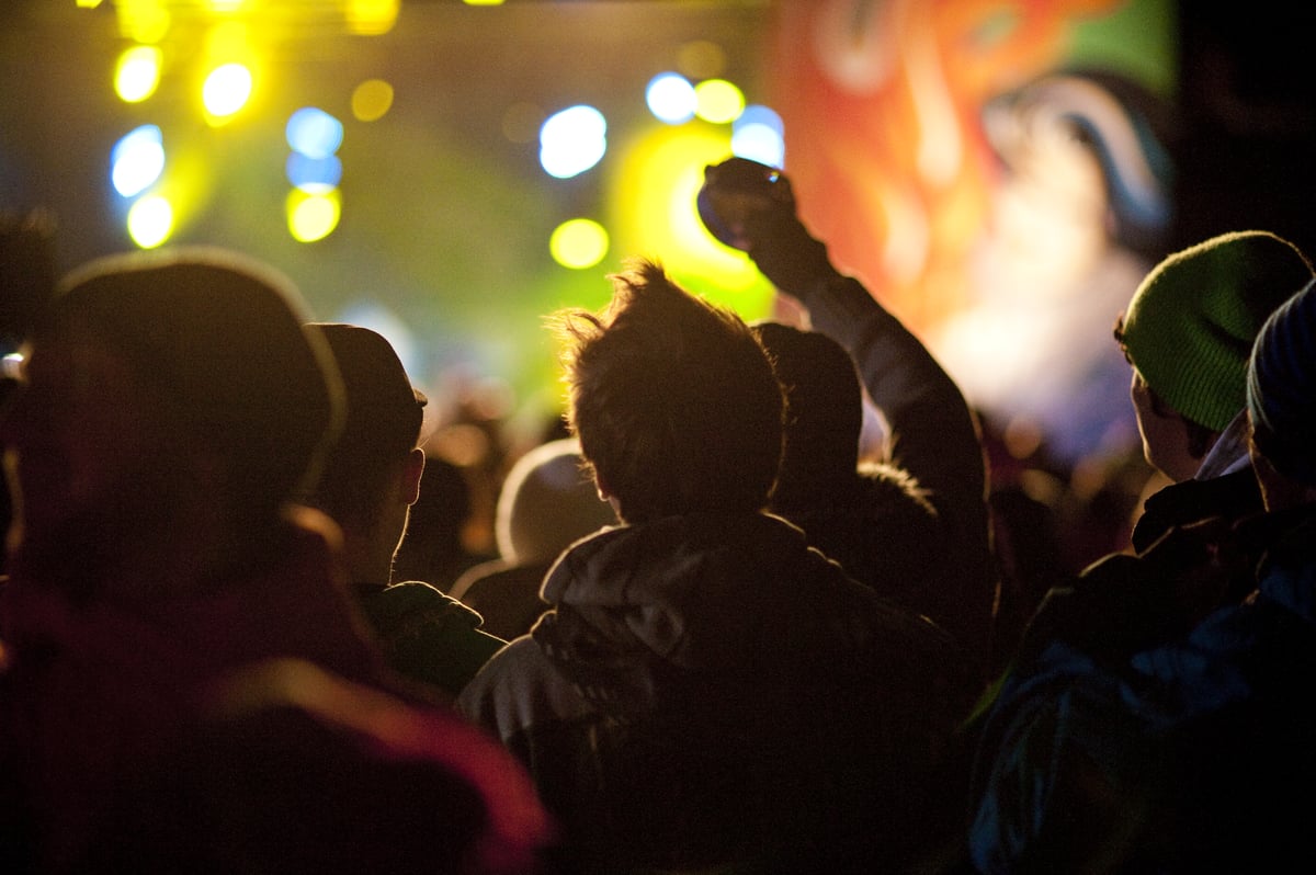 A crowd of people watches a live performance with lights and projections.