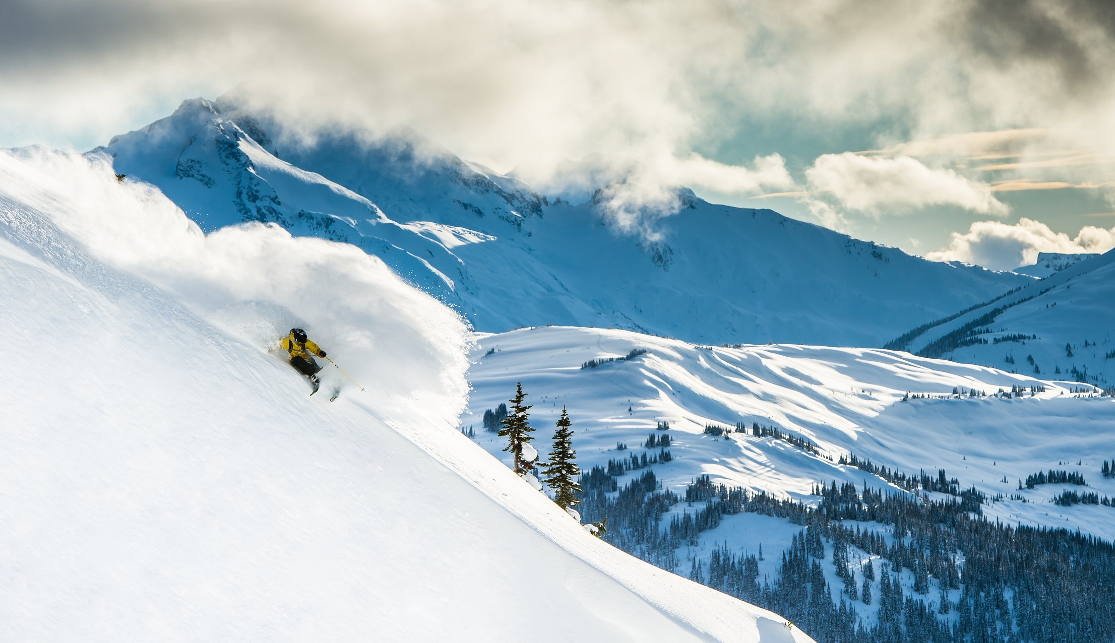 A skier glides through deep powder in Whistler with the Coast Mountain range in the backdrop.