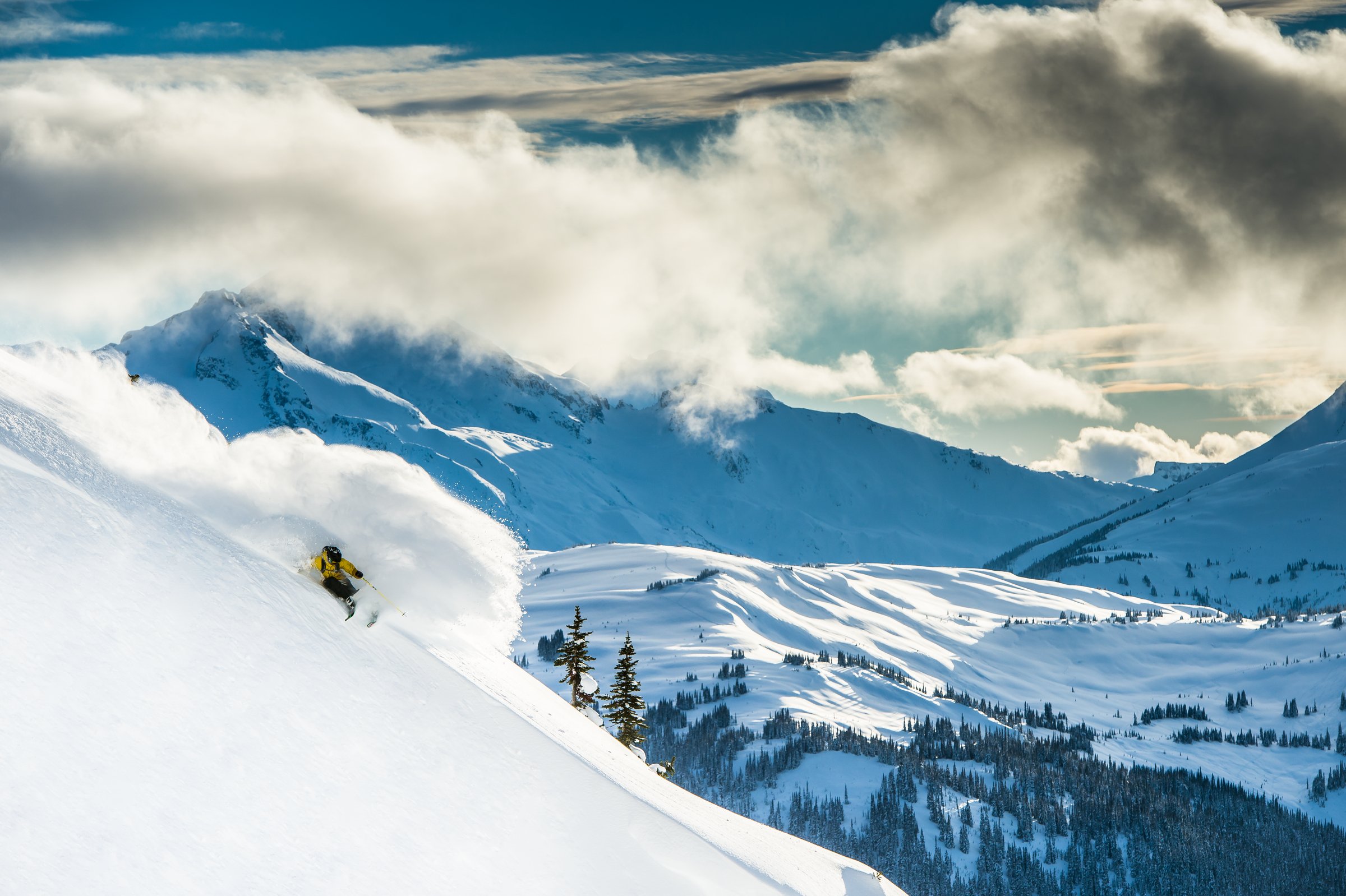 A skier glides through deep powder in Whistler with the Coast Mountain range in the backdrop.