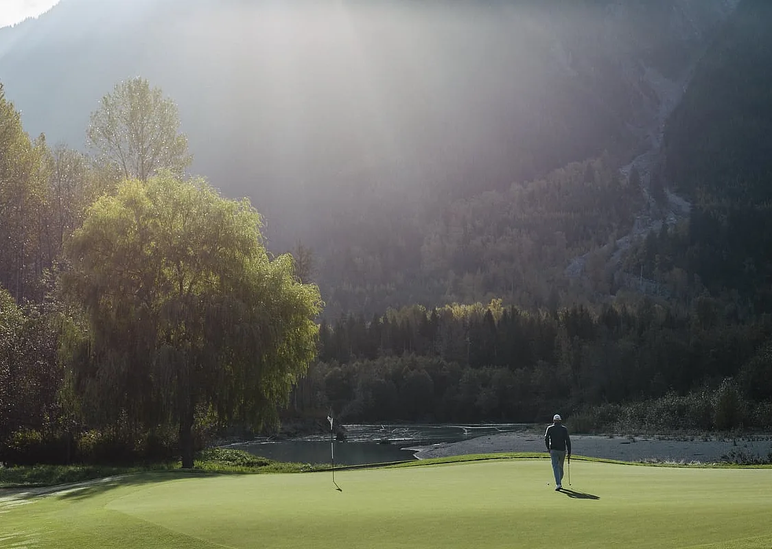 A golfer on the green looking up at the mountains at Big Sky Golf Club