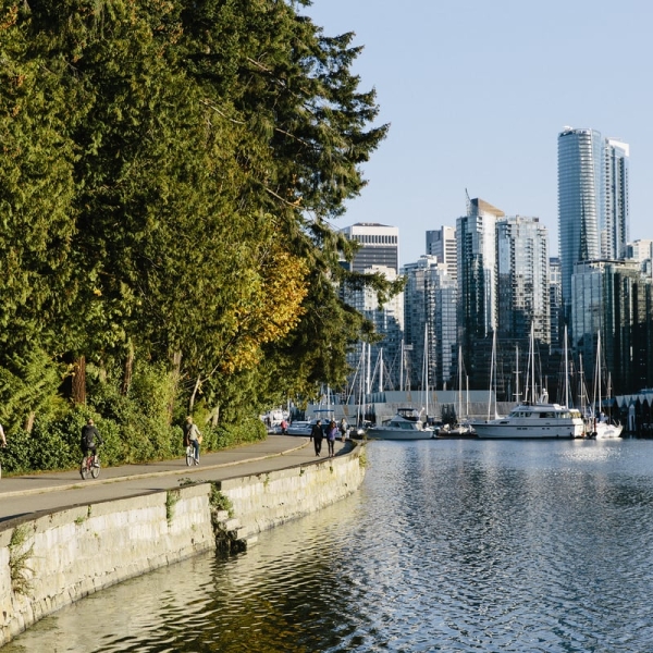 People walk along the seawall in Stanley Park in the summer time. Downtown Vancouver is seen in the background across the water.