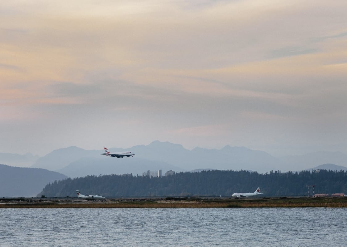 Un avión aterriza en el Aeropuerto Internacional de Vancouver. La foto está tomada desde el otro lado del río Fraser, y las montañas North Shore son visibles de fondo.