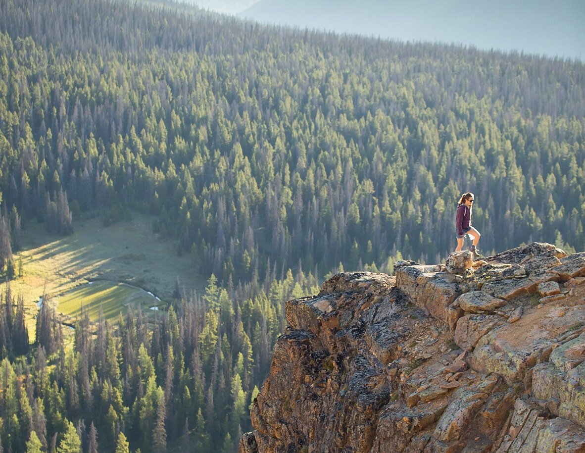 A person stands on a rock ledge looking out at the views below in Cathedral Provincial Park